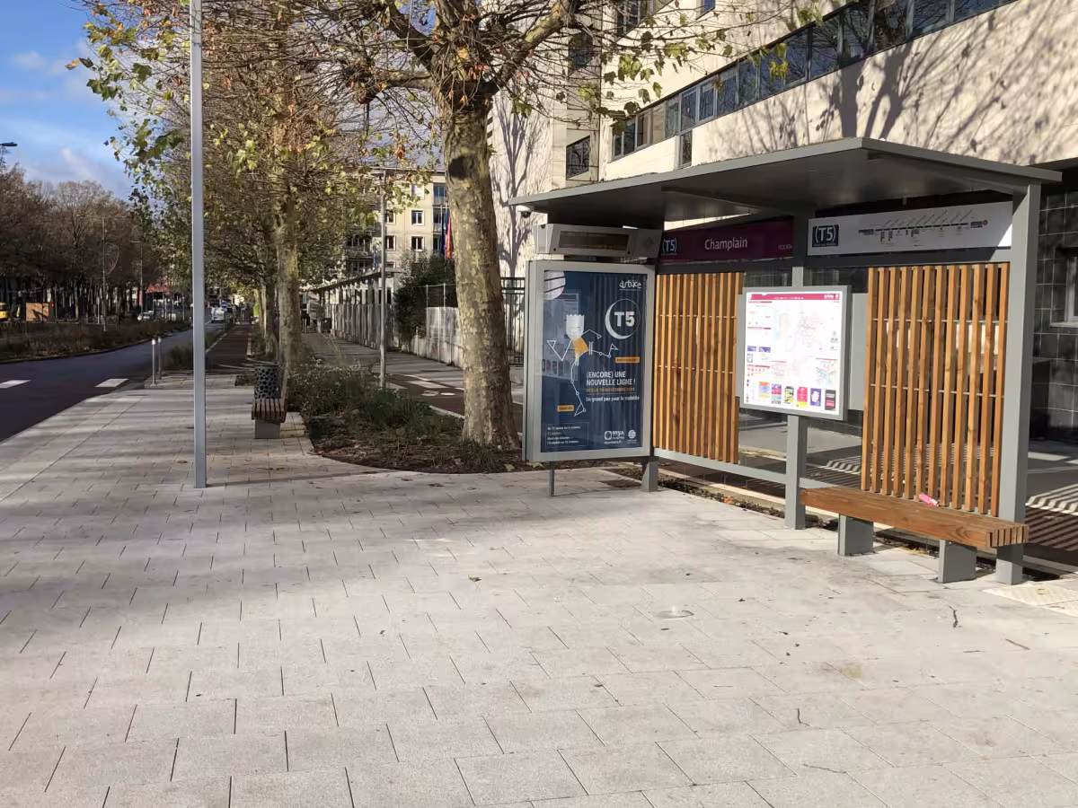 Arrêt de tramway Champlain (ligne T5) avec abri voyageurs, panneau d’information et avenue arborée.