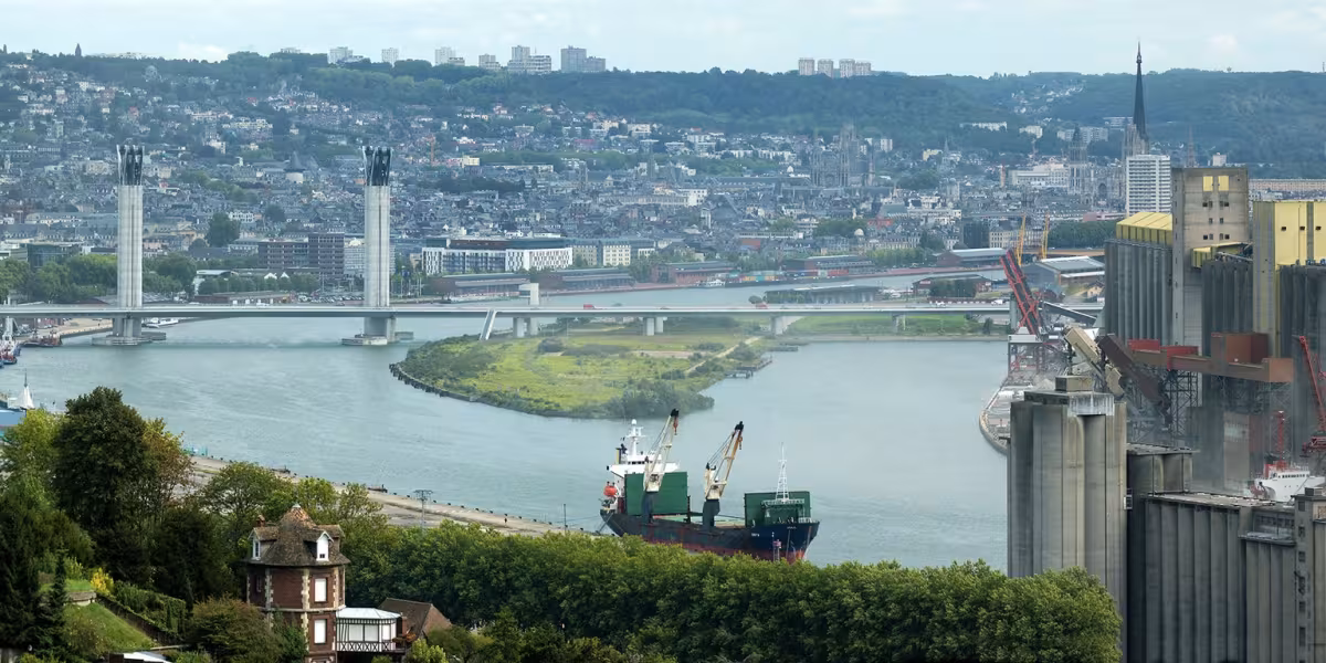 Vue d’une ville traversée par une rivière avec ponts, bateau et installations portuaires.
